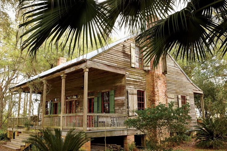 an old house in the woods with palm trees and stairs leading up to it's porch