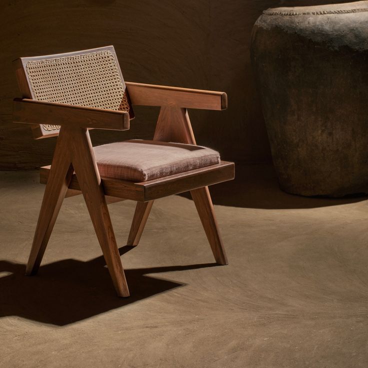 a wooden chair sitting in front of a large stone vase on top of a floor