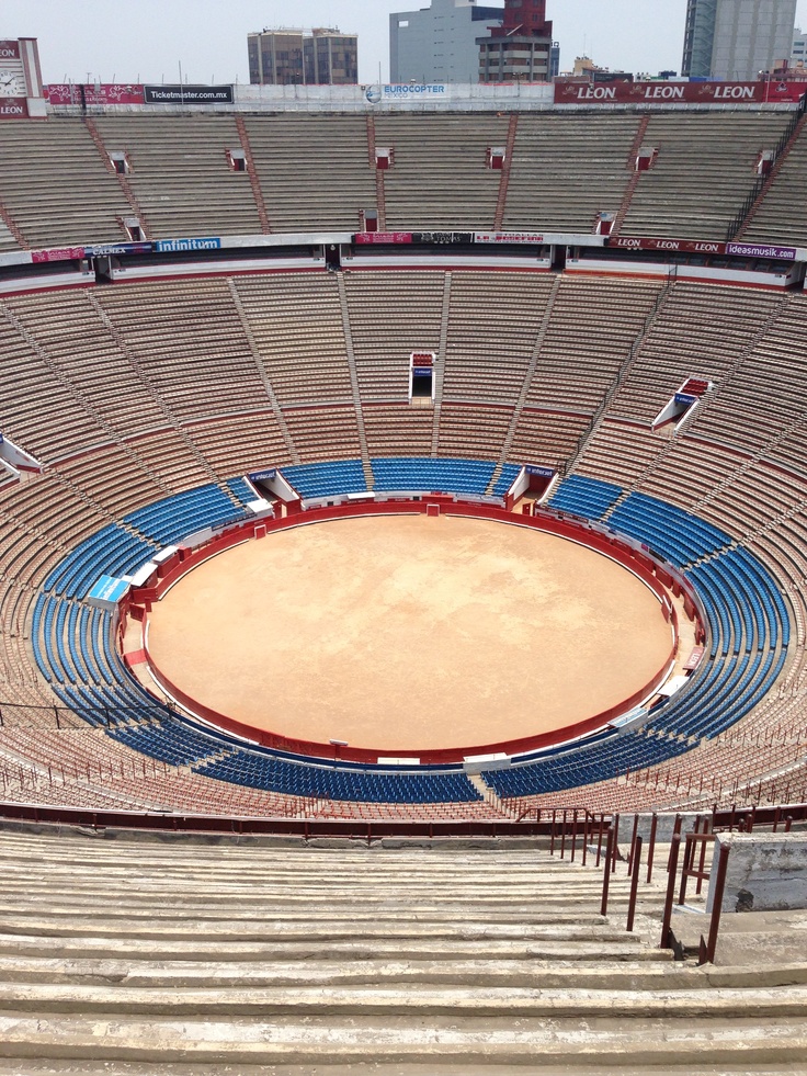 an empty stadium with blue seats and a large brown bull ring in the foreground