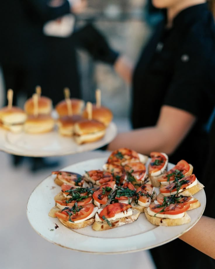 two plates with mini sandwiches on them, one being held by a woman's hand