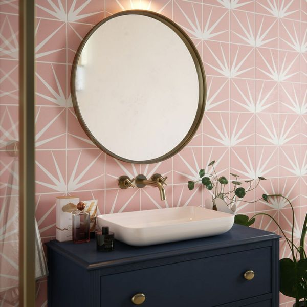 a bathroom with pink wallpaper and a round mirror above the sink on top of a dresser