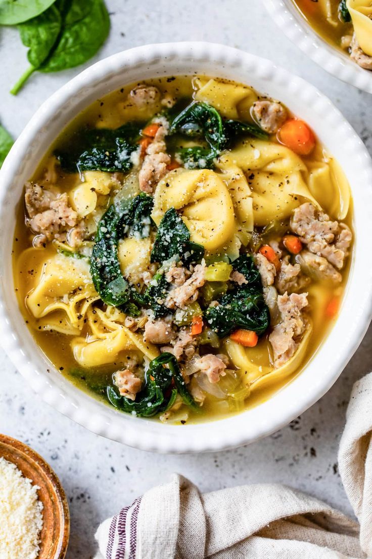 two bowls filled with pasta, meat and spinach soup on top of a table