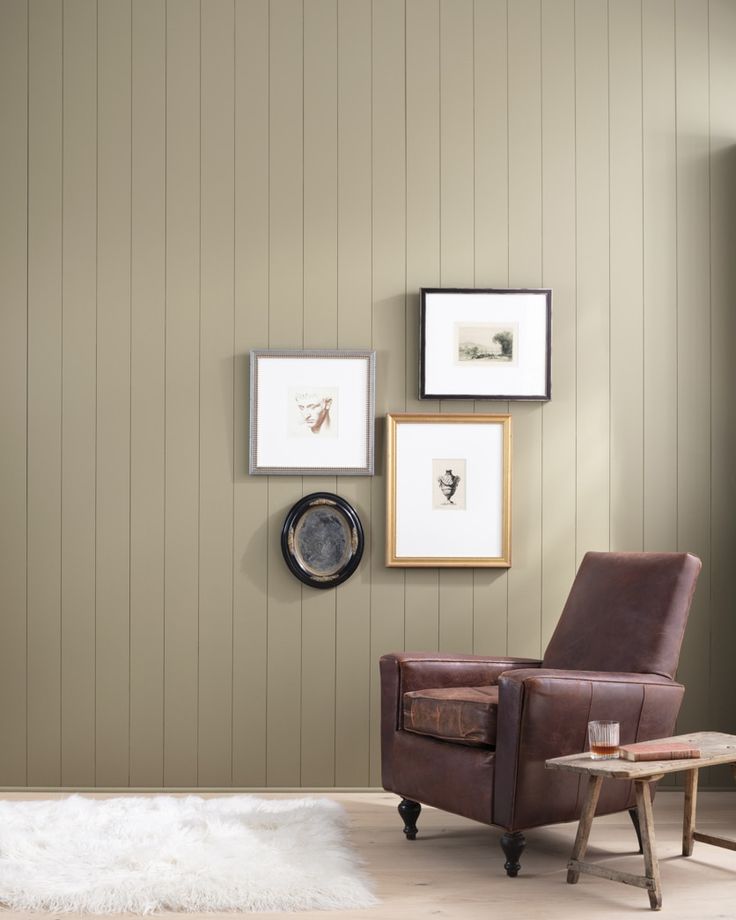 a brown chair sitting in front of a wall with pictures on the wall above it