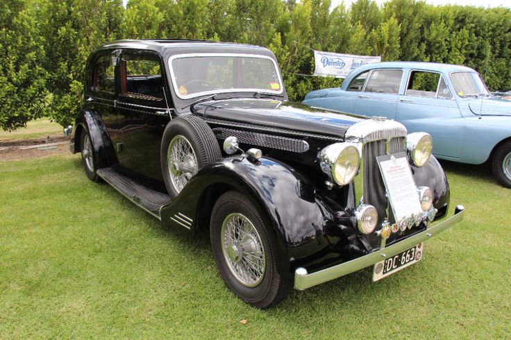 an old black car parked on top of a lush green field next to another blue car