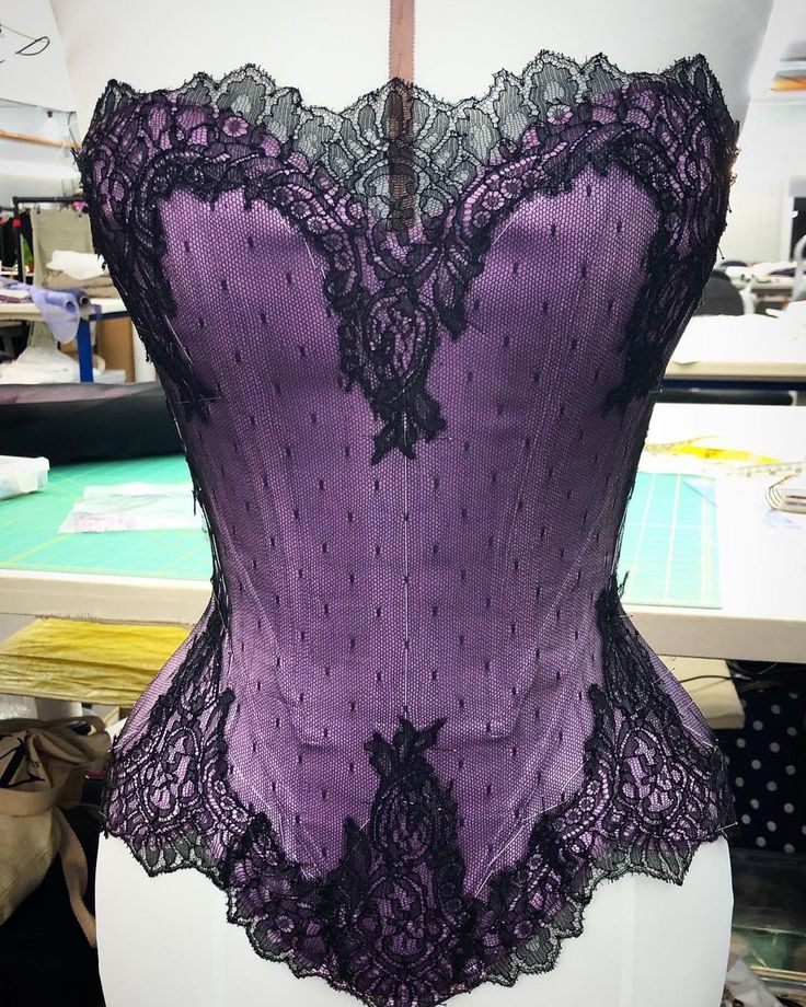 a purple corset with black lace on the top and bottom, sitting on a mannequin