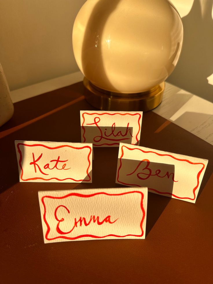 three pieces of paper with red writing on them sitting next to a vase and lamp