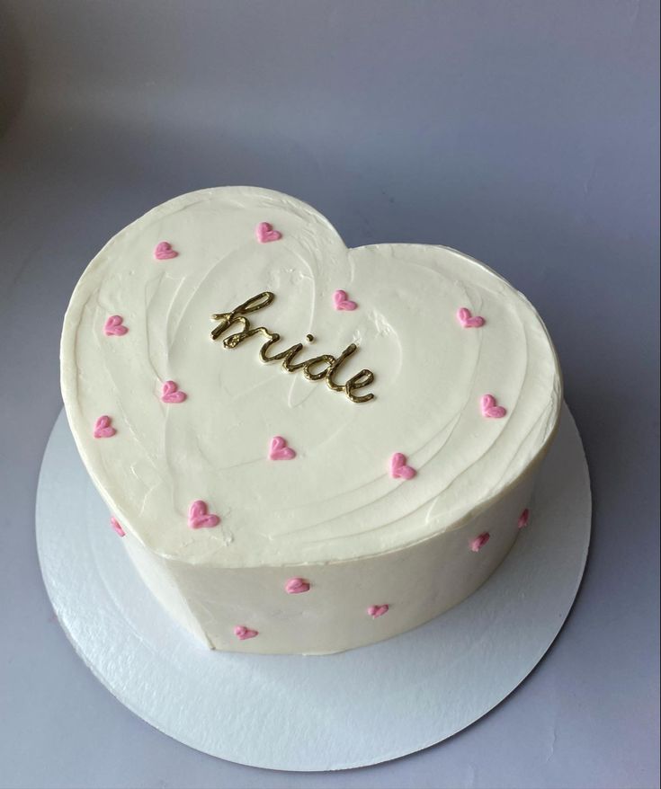 a white heart shaped cake with pink hearts on it and the word bride spelled in gold