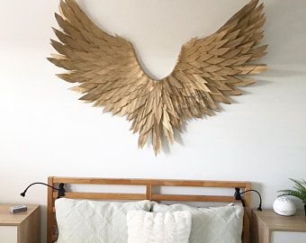 a bed with white sheets and pillows in front of a large gold angel wings wall decoration