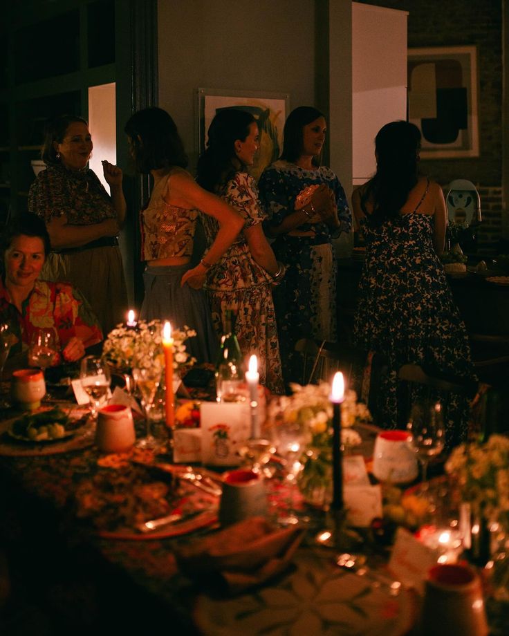 a group of people standing around a table with candles on it and plates full of food