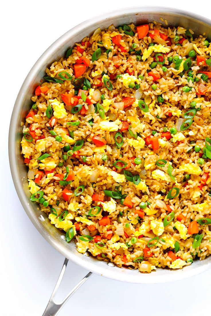 a pan filled with rice and vegetables on top of a white table next to a fork