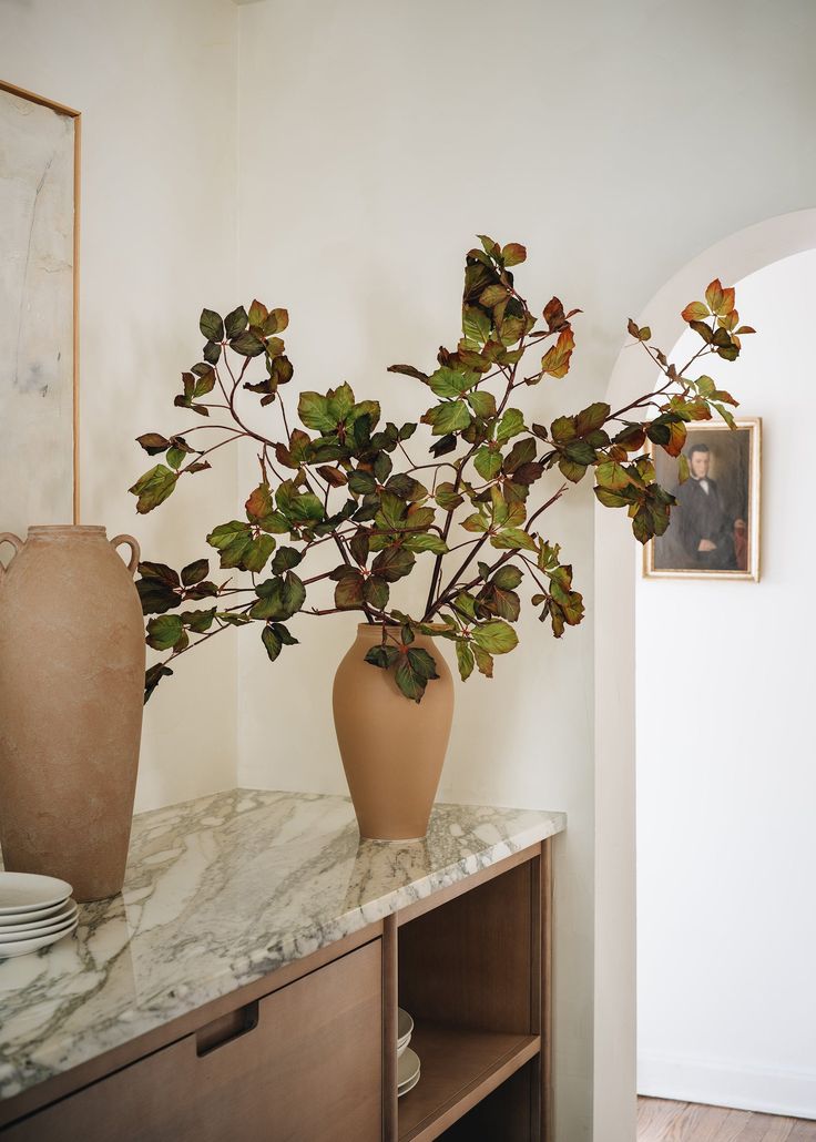 a vase filled with green leaves sitting on top of a table next to a wall