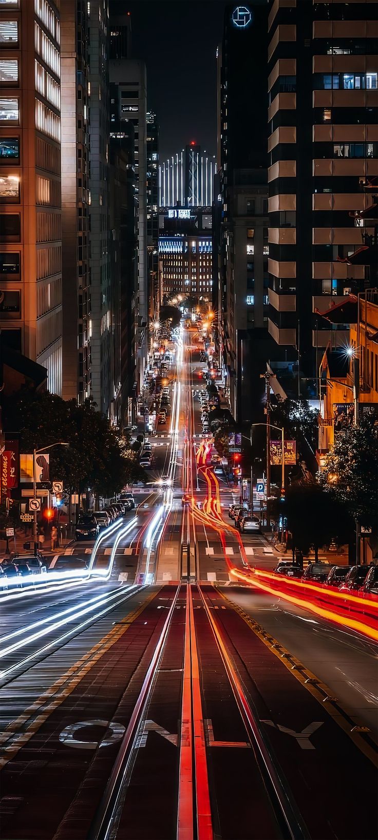 the city street is lit up at night with light streaks on it and buildings in the background