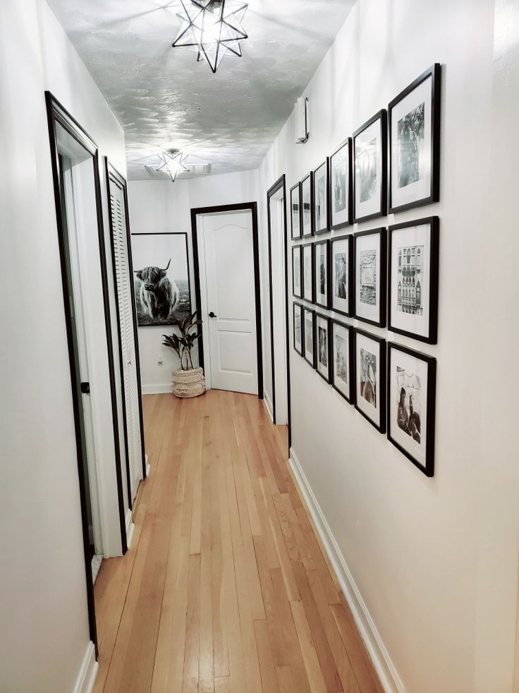 an empty hallway with pictures on the wall and wooden flooring, along with framed photographs