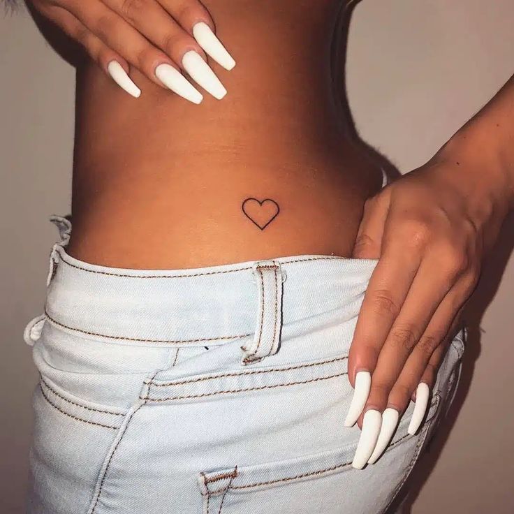 a woman's stomach with white nails and a heart tattoo on her left side