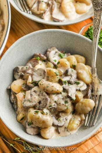 a bowl filled with pasta and mushrooms on top of a wooden table next to silverware