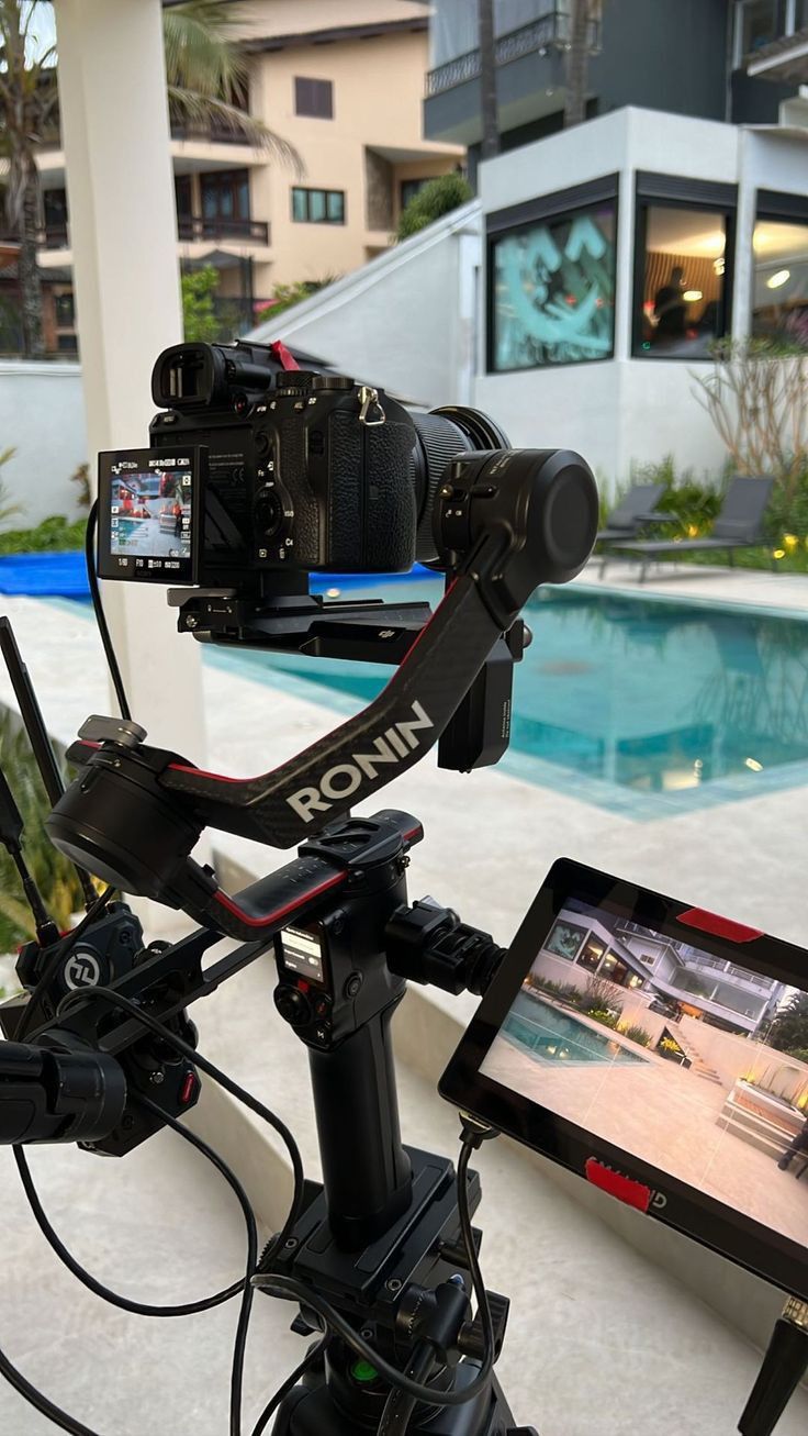 a video camera attached to a tripod next to a swimming pool with a house in the background