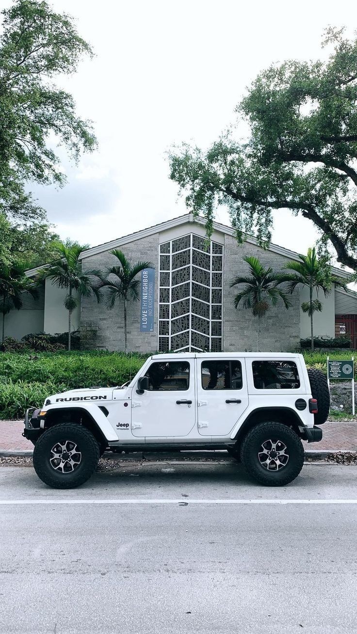 a white jeep is parked in front of a building with trees and bushes around it