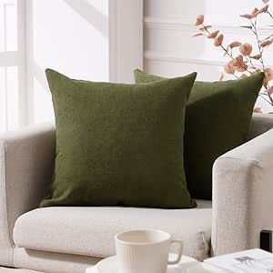 a white couch with two green pillows and a coffee cup on the table next to it