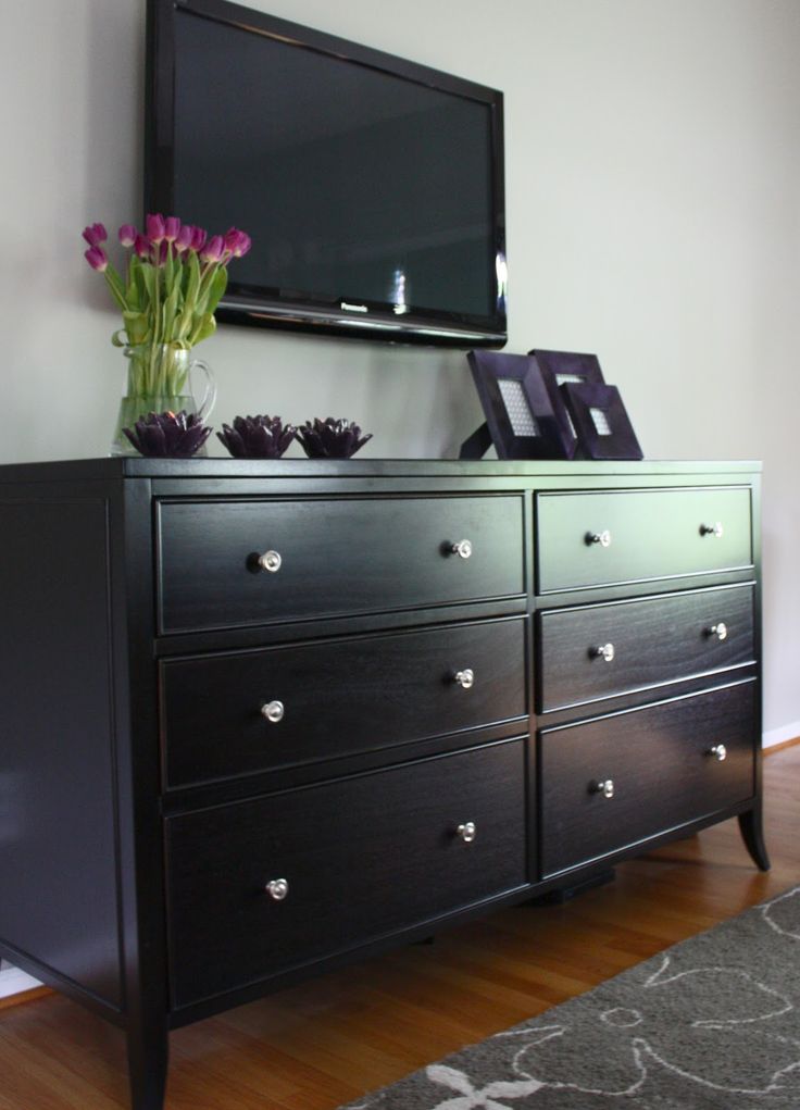 a black dresser with flowers on top and a flat screen tv mounted above the dresser