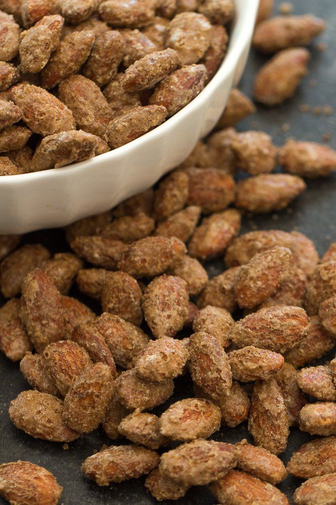 a white bowl filled with nuts sitting on top of a black counter next to a pile of peanuts