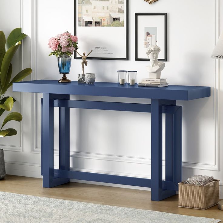 a blue console table with vases and pictures on the wall in front of it