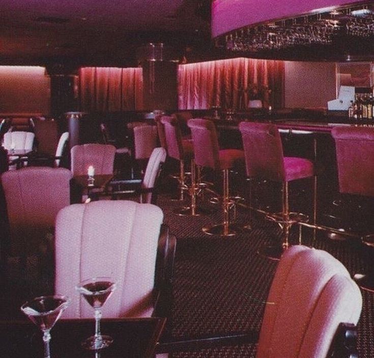 the interior of a restaurant with pink and black chairs, bar stools, and wine glasses