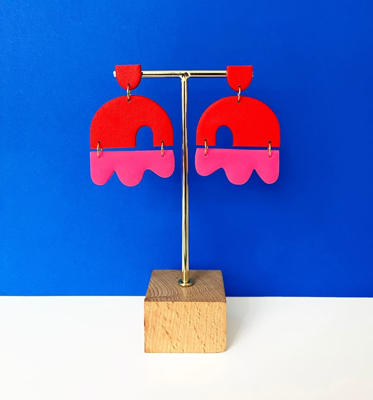 a pair of pink and red earrings sitting on top of a wooden block in front of a blue wall