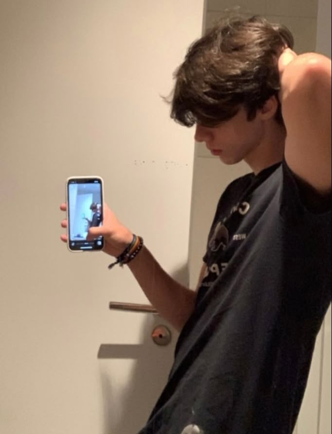 a young man holding up his cell phone to take a selfie in the mirror