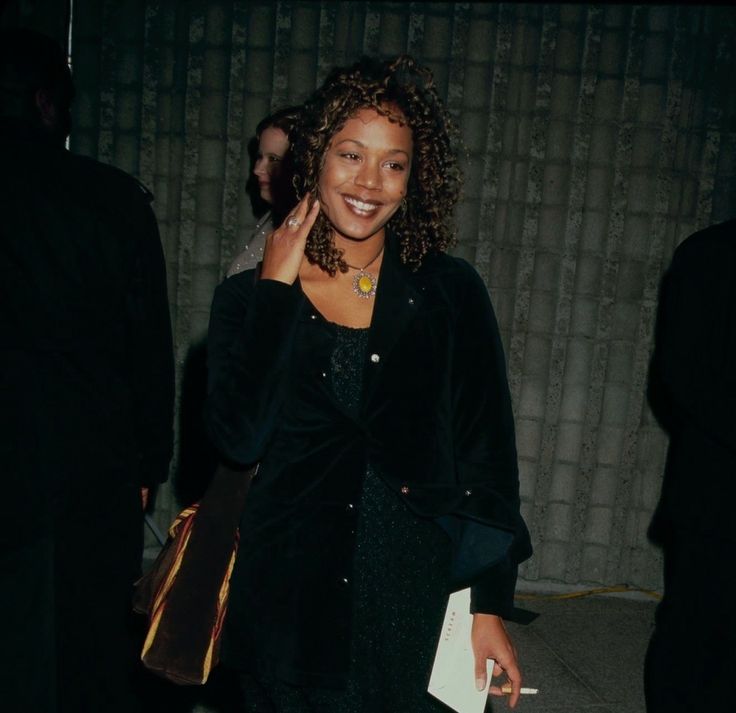 a woman in a black dress is talking on her cell phone and smiling at the camera