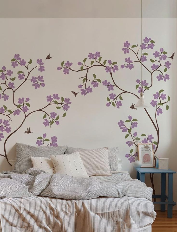 a bed sitting under a wall with purple flowers painted on it's sides and two birds flying over the branches