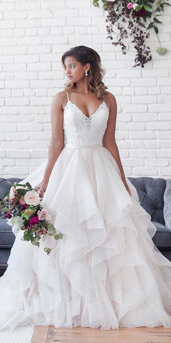 a woman standing in front of a couch wearing a wedding dress and holding a bouquet