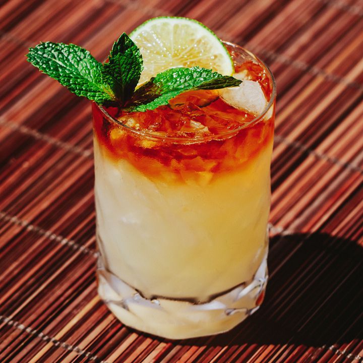 a drink with ice, lemon and mint garnish sitting on a bamboo mat