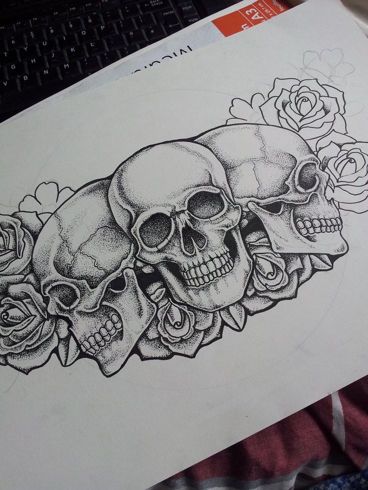 a drawing of three skulls and roses on a sheet of paper next to a laptop