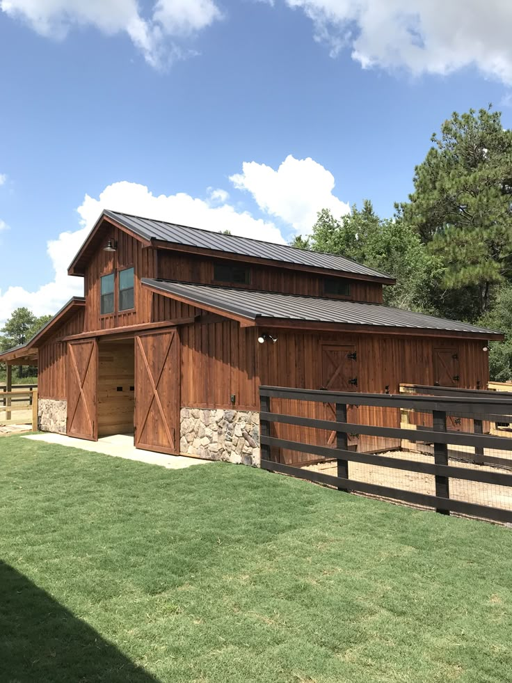 a barn with a horse pen in front of it and grass around the yard area