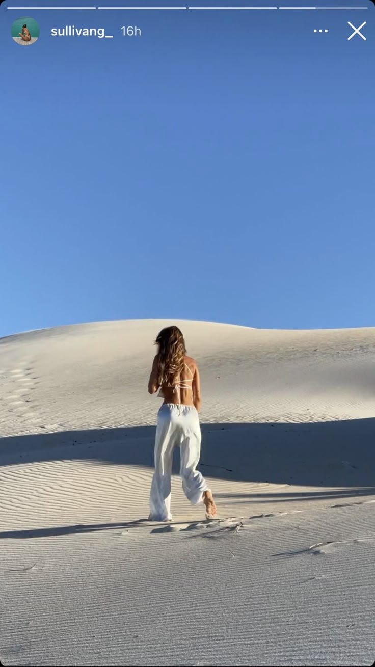 a woman in white pants walking across a desert