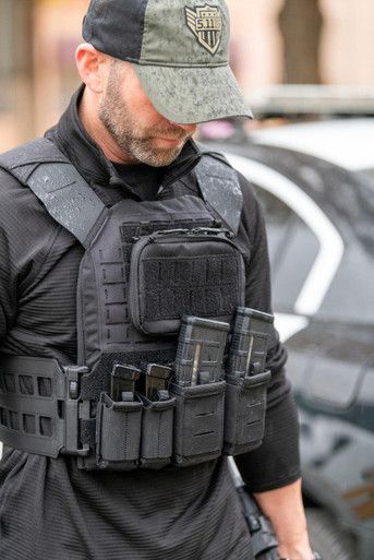 a man wearing a black vest and hat walking down the street with his hands in his pockets