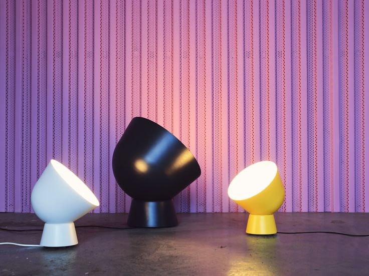 three different colored lamps sitting next to each other on a floor in front of a purple wall