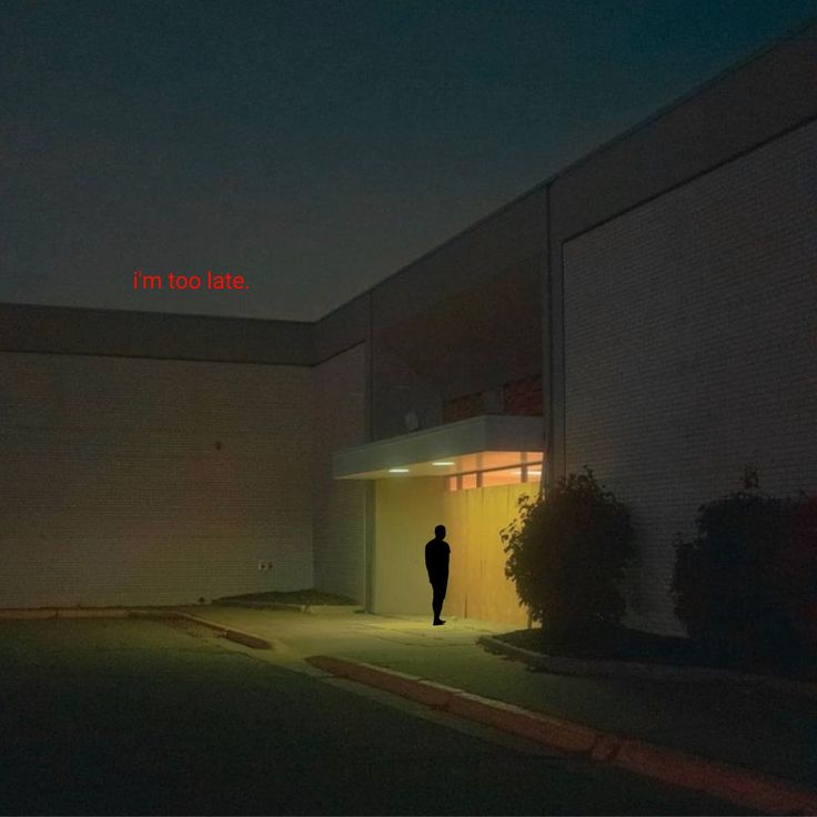 a person standing in front of a building at night with the word i'm too late written on it