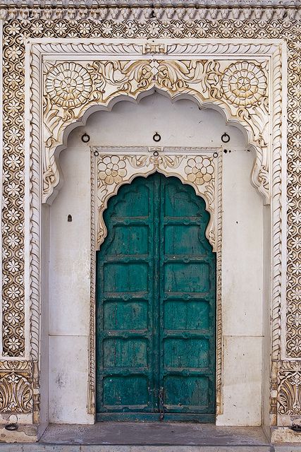 an image of a green door in front of a white wall with carvings on it