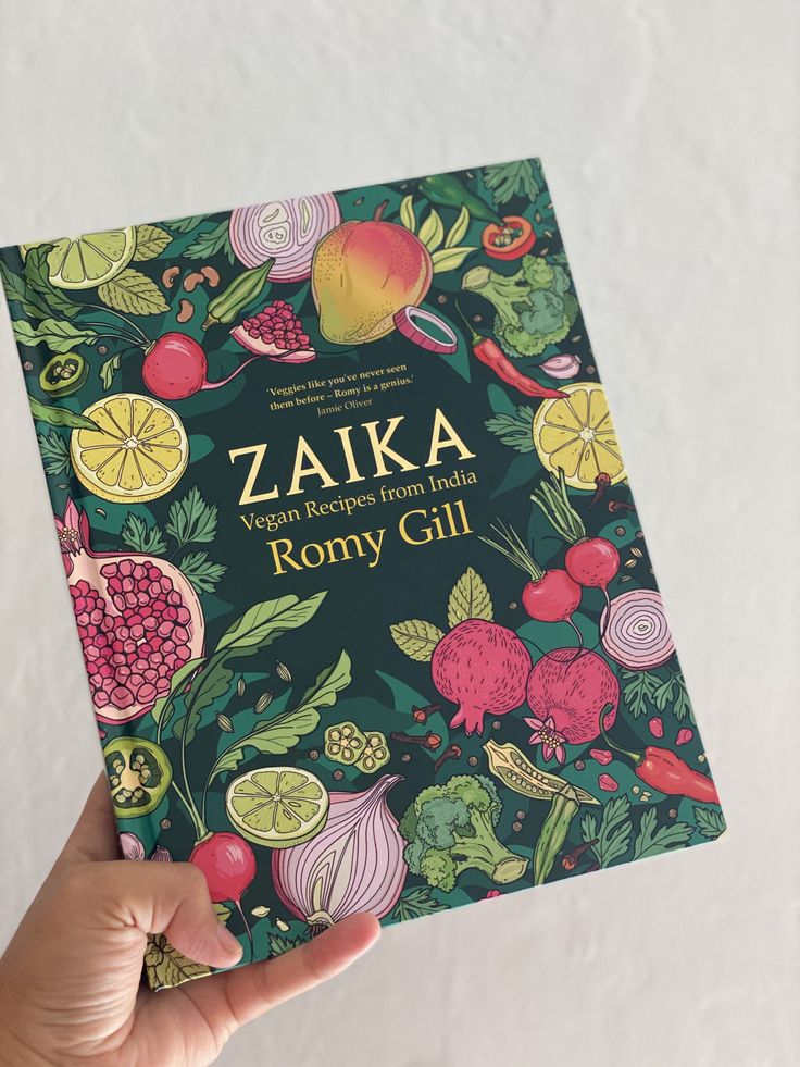 a person holding up a book in front of a white wall with fruit and vegetables on it