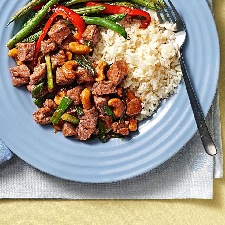 a blue plate topped with meat and veggies next to rice on a table