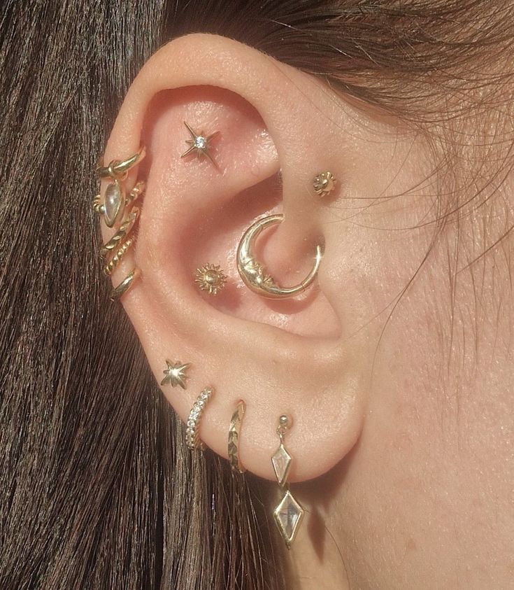 a close up of a person's ear with multiple piercings on it, including stars and moon