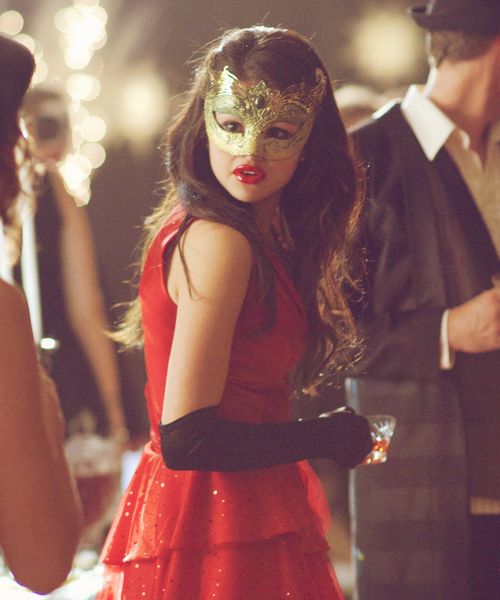 a woman in a red dress and mask standing next to other people at a party