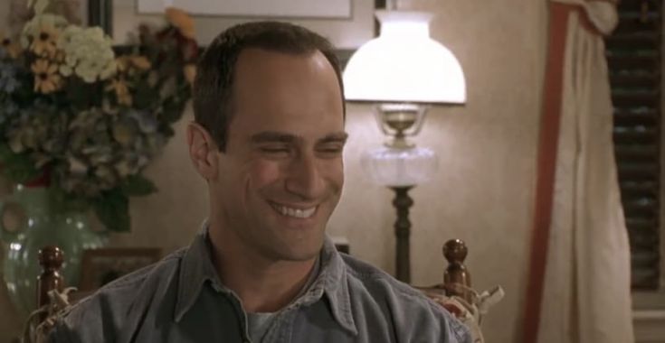 a man sitting in a chair smiling at the camera with flowers on the wall behind him