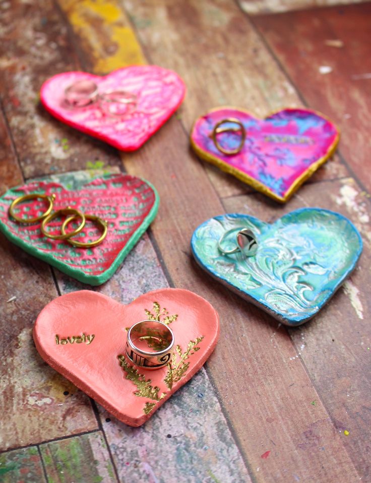 three heart shaped trays with wedding rings on them sitting on a wooden floor next to each other