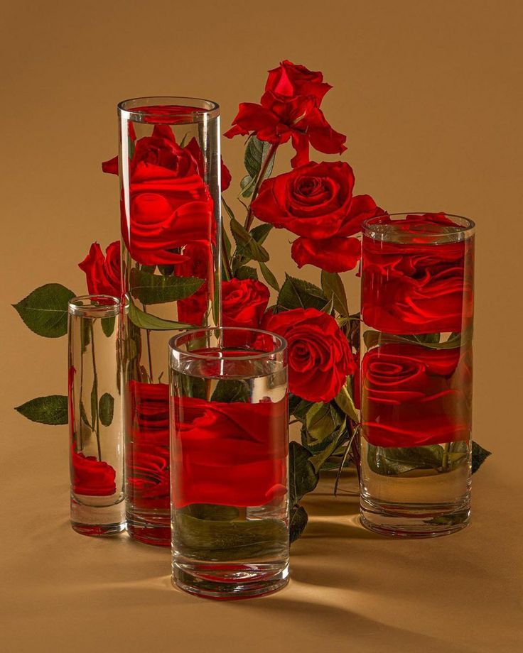 several vases with red roses in them on a brown background, one is empty and the other two are half full