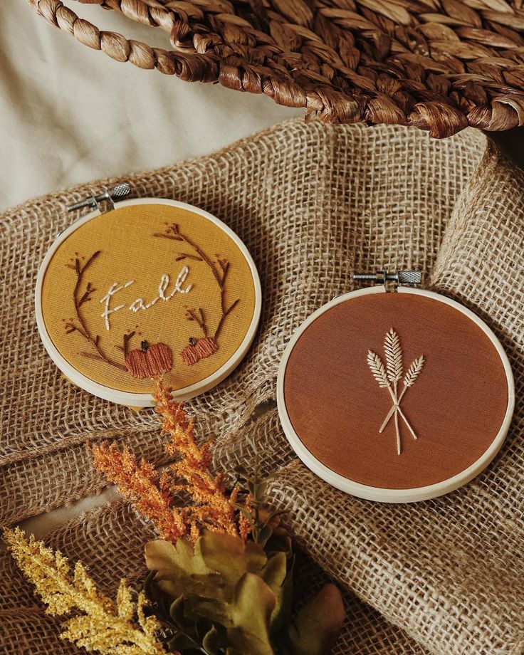 two cross stitch hoops sitting next to each other on top of a cloth covered table