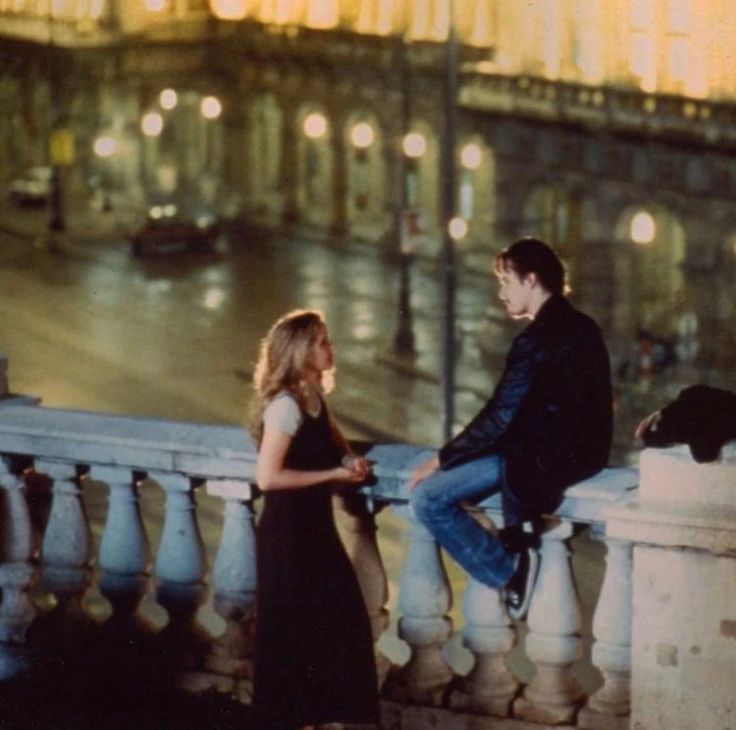 a man and woman are sitting on a balcony in the rain looking at each other