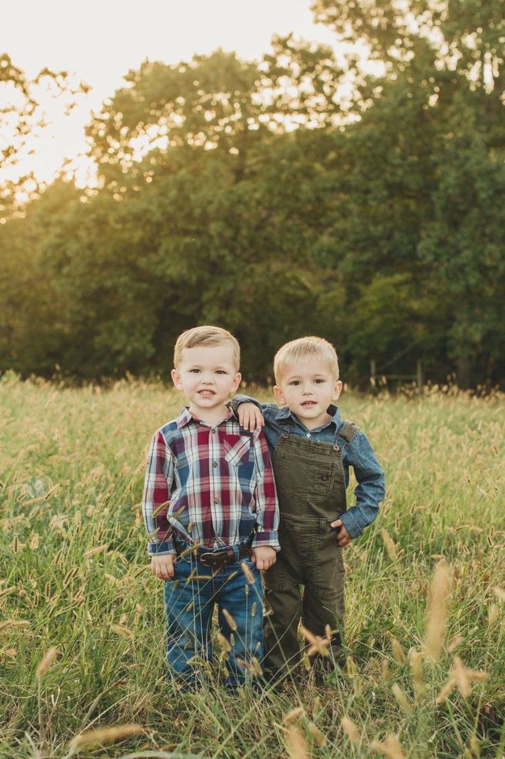 two young boys standing in tall grass with trees in the backgrouds behind them