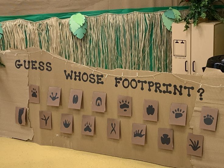 a cardboard board with handprints on it and grass growing over the top that says guess who's footprints?